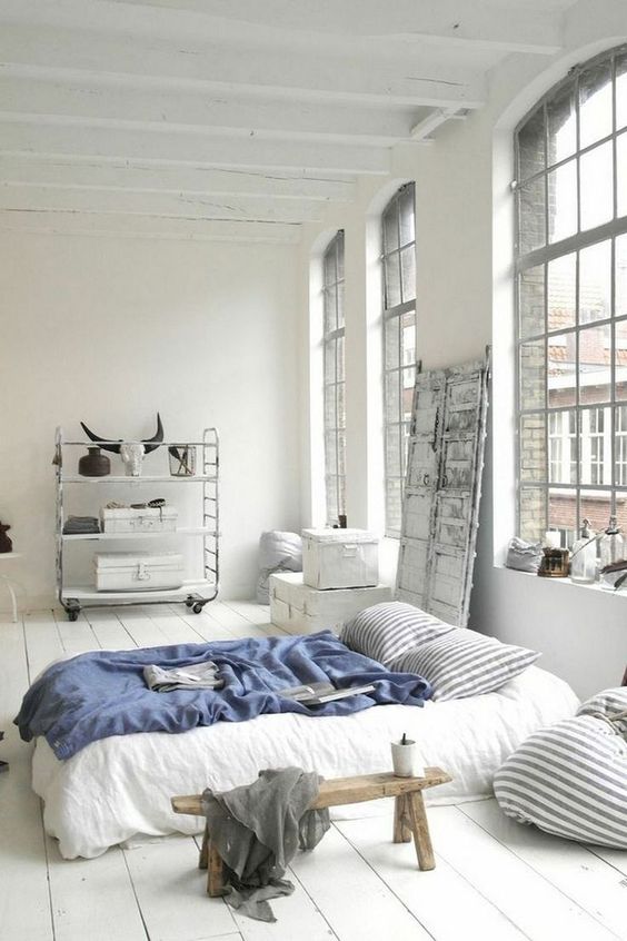 a Scandinavian sleeping space with oversized windows, a shelving unit on casters, a comfy bed and some wooden furniture