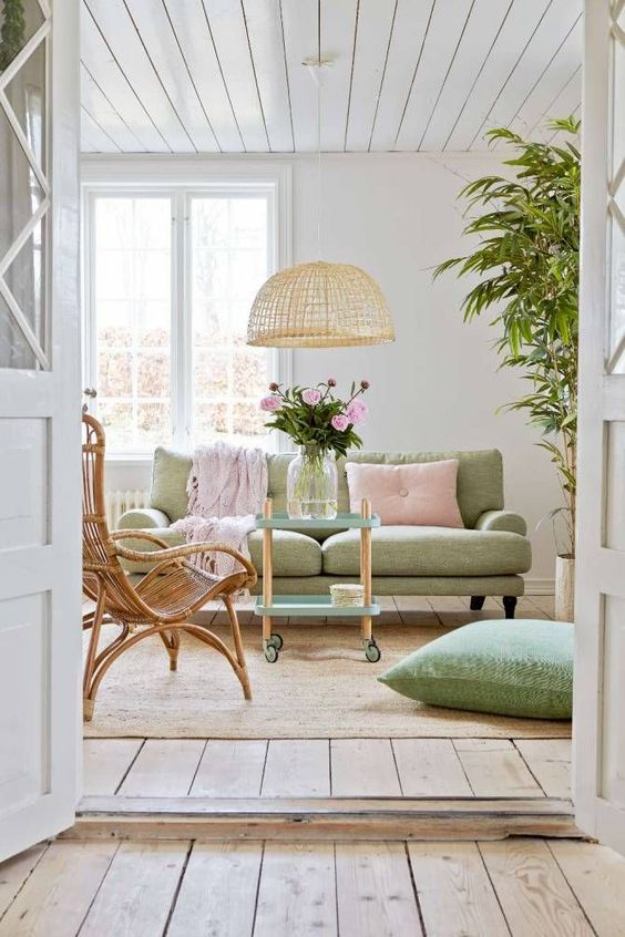 a beautiful pastel living room with a light green sofa and a pillow, a pink pillow and a blanket, a wicker lamp and a rattan chair