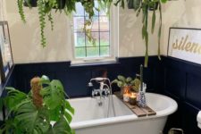 a bold navy and neutral bathroom with a tile floor, paneling and lots of potted green plants around the tub