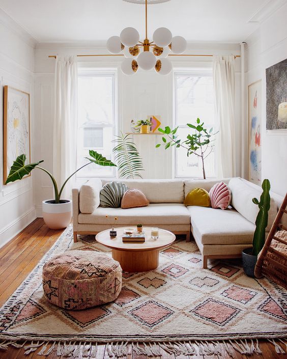 a bright and chic modern living room with a neutral sofa, a boho rug and ottoman, pastel pillows and potted plants