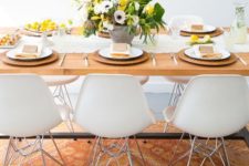 a bright and fresh spring table setting with a yellow and spring floral centerpiece, wicker chargers, a white runner and yellow napkins