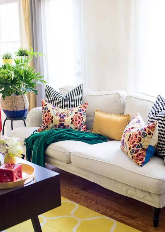 a bright living room with a white sofa accented with bright pillows, a bold rug and a dark coffee table plus greenery