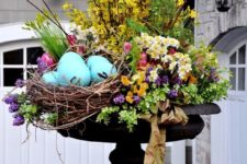 a bright outdoor Easter arrangement with yellow, purple, pink blooms, greenery and large fake blue eggs
