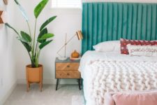 a bright spring bedroom with a turquoise bed, a pink bench, potted greenery and artworks already feels like spring itself