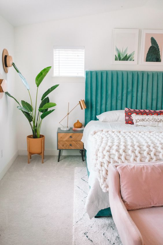 a bright spring bedroom with a turquoise bed, a pink bench, potted greenery and artworks already feels like spring itself