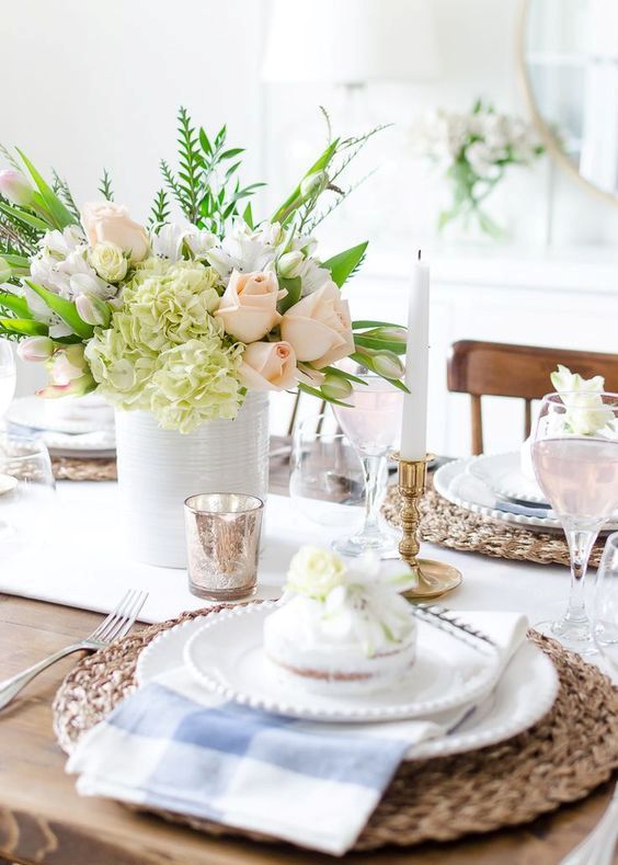 a bright spring tablescape with wicker chargers, checked napkins, a pastel floral centerpiece and some mercury glass accessories