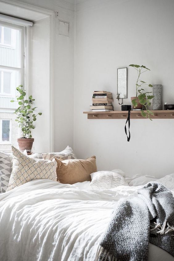 a charming bedroom with a bed, an open shelf, some greenery in pots and neutral bedding