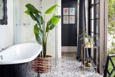 a chic monochromatic bathroom with a tile floor, a black tub and chair and a statement plant ina  wicker pot