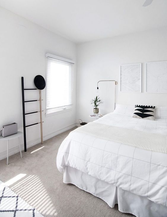 A clean Nordic bedroom with a white bed, artworks, a ladder, lamps and a stool   blakc for drama