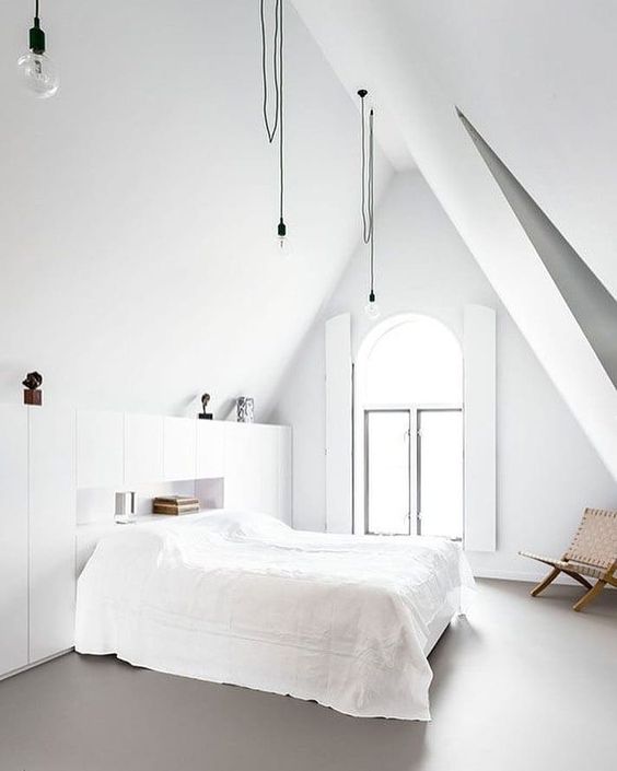 a clean Nordic bedroom with an arched window, hanging bulbs, storage units, a bed and a wicker chair