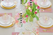 a colorful spring table setting with pink napkins, a floral table runner, wooden beads and striped candles plus pink glass