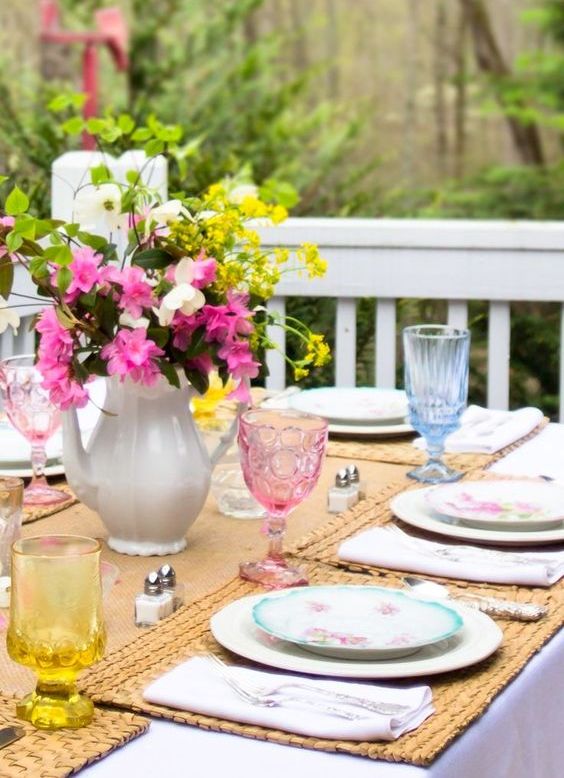 a colorful spring tablescape with bright glasses, a bright floral centerpiece, woven placemats and a runner