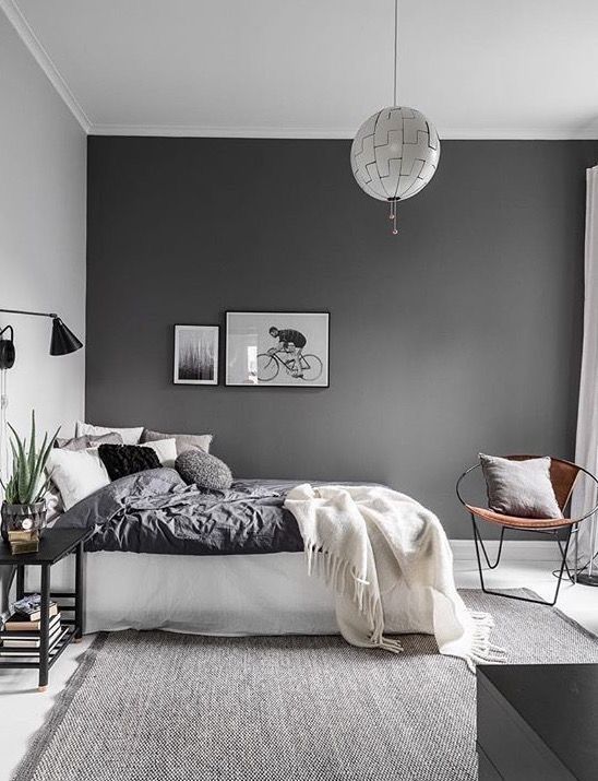 a contemporayr Scandinavian bedroom with a dark wall, monochromatic bedding, lamps and lights and a grey rug