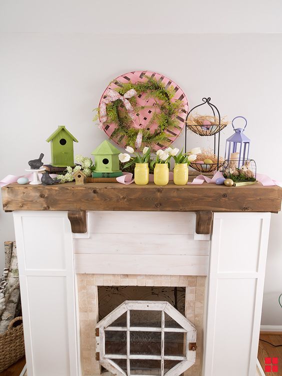a cozy Easter mantel with green bird houses, yellow jars with blush tulips, faux eggs and nests and a pink basket with greenery