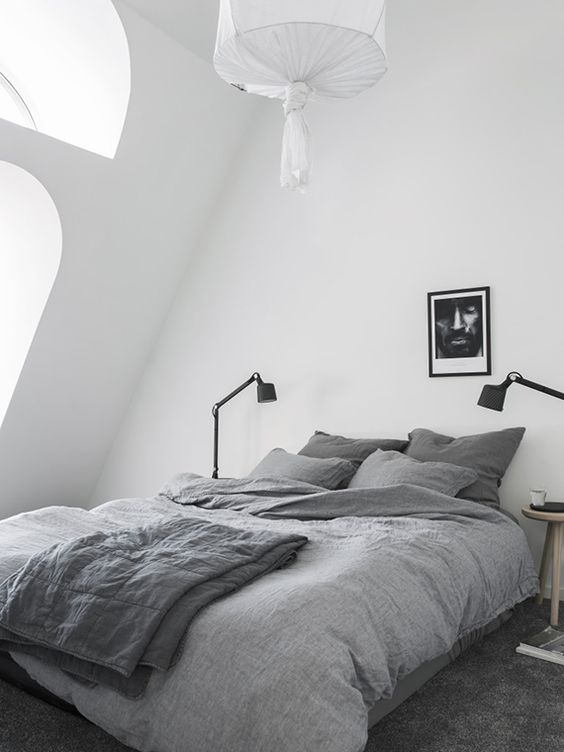 a cozy attic Nordic bedroom with arched windows, a bed, table lamps, an artwork and a pendant lamp