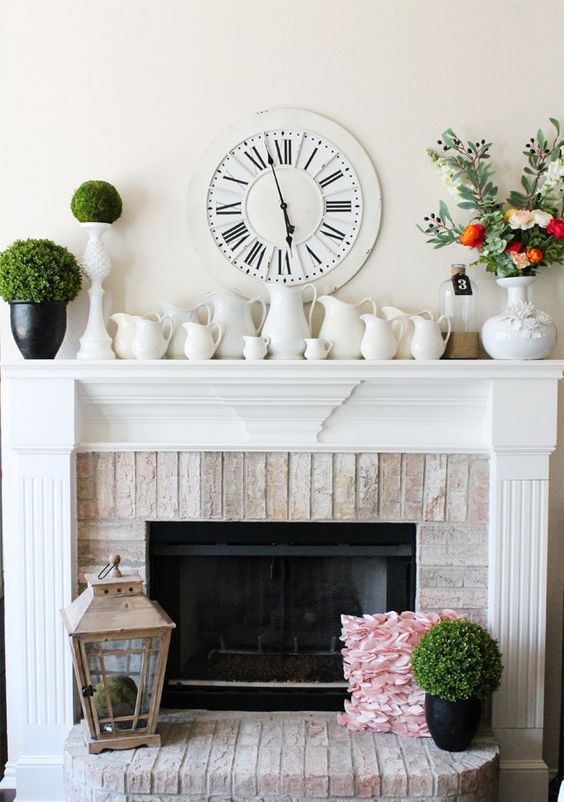 a farmhouse spring mantel with lots of vintage jugs, green topiaries, a moss ball in a lantern and a fresh flower arrangement