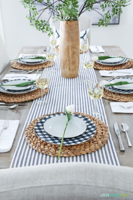 a fresh modern spring table setting with a striped table runner, checked plates, wicker chargers, greenery and white tulips