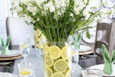 a fresh modern spring tablescape with a white floral centerpiece with lemon slices, wicker chargers, printed bunny napkins