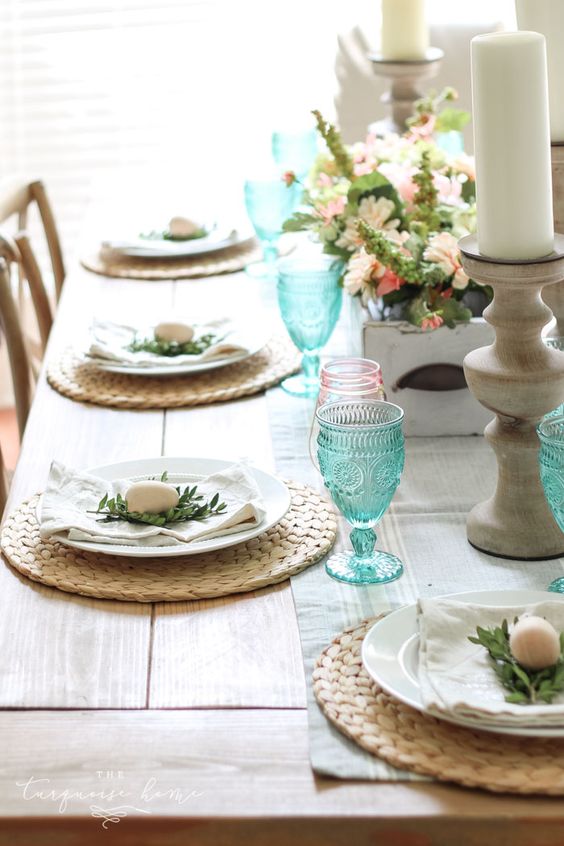 a fresh spring table with wicker chargers, blue and pink glasses, little eggs and greenery plus a lush centerpiece