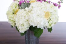 a metal bucket with white hydrangeas, pink blooms, succulents and lemons in it