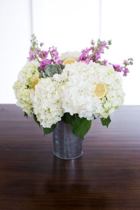 a metal bucket with white hydrangeas, pink blooms, succulents and lemons in it