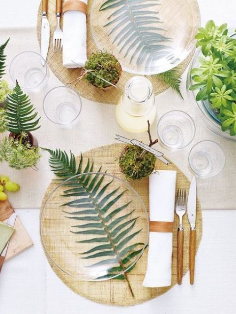 a modern spring table setting with wooden placemats, much fresh greenery and moss, candles and wooden cutlery