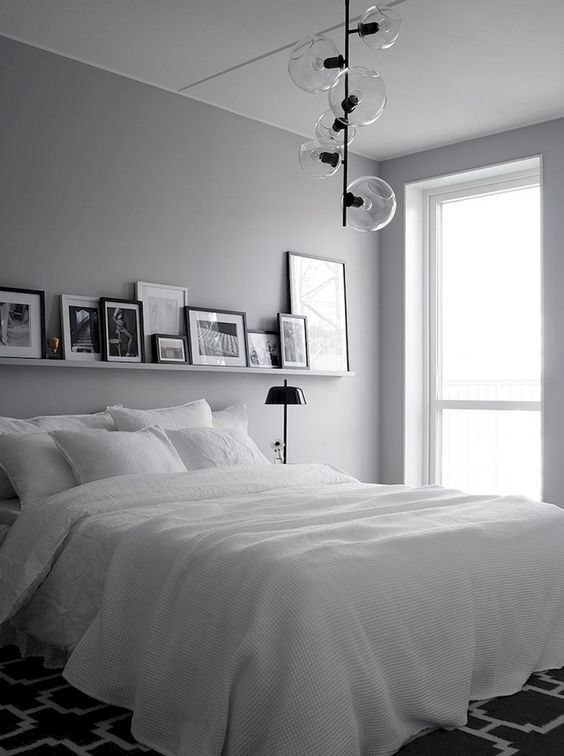 a monochromatic Nordic bedroom with hanging lamps, a white bed, a ledge with artworks and black lamps