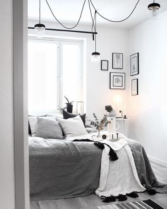 a monochromatic Scandi bedroom with a bed with grey and white bedding, some lamps, lights and a gallery wall