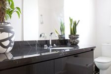 a monochromatic bathroom with a black stone vanity and succulents and a statement climbing plant on the wall