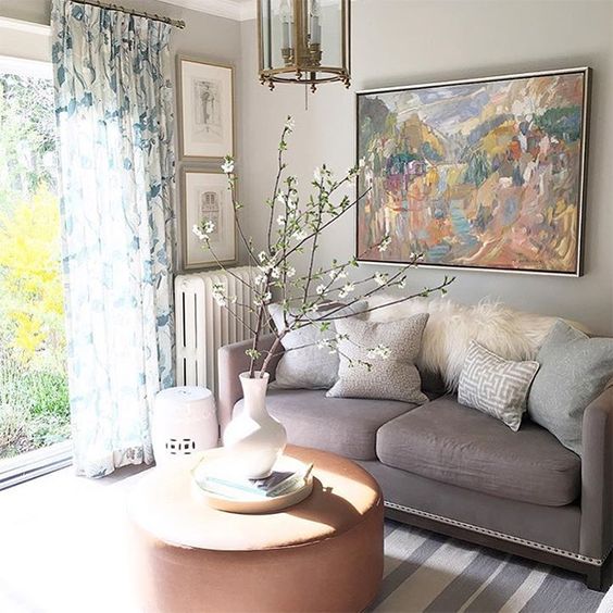a neutral and pastel living room with grey walls and a sofa, blue touches, floral curtains and a striped rug plus blooming branches
