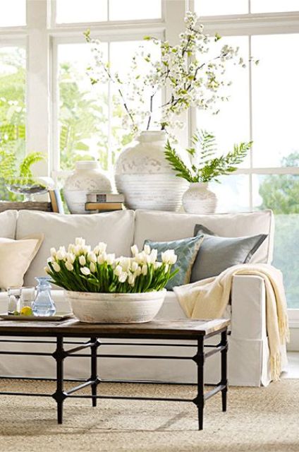 A neutral and pastel living room with potted greenery and blooms, with printed vases and a glazed wall is fresh and spring like
