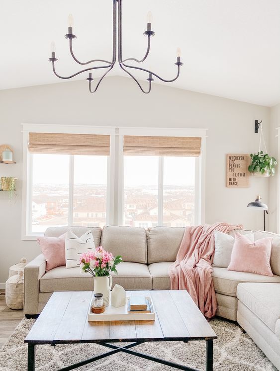 a neutral farhouse livng room with light pink linens, potted greenery and blooms and a printed rug is welcoming