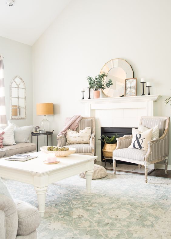 a neutral farmhouse living room with printed chairs and a printed rug, potted greenery, pink linens and mirrors