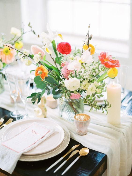 a neutral runner, a colorful floral centerpiece, candles, gilded cutlery and pastel plates for a vibrant look