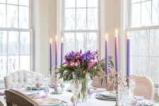 a refined colorful spring tablescape with a bright floral centerpiece, purple candles, printed plates and chargers