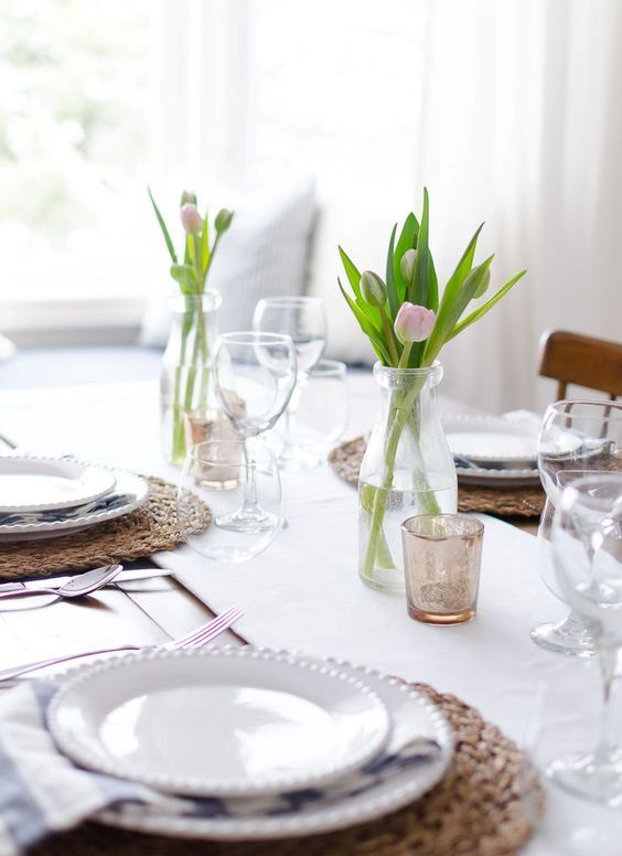 a simple and modern wedidng tablescape with a white table runner, tulip centerpieces, wicker chargers and white porcelain