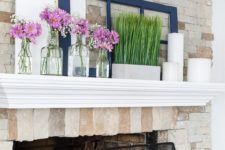 a simple spring mantel with grass in a pot, pillar candles and some pink floral arrangements in clear vases