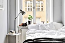 a small Nordic bedroom with a bed, a nighstand with a lamp, potted greenery and grey walls