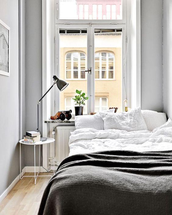 a small Nordic bedroom with a bed, a nighstand with a lamp, potted greenery and grey walls