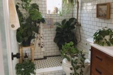 a small and neutral bathroom with a wooden vanity, lots of greenery in pots and some suspended plants