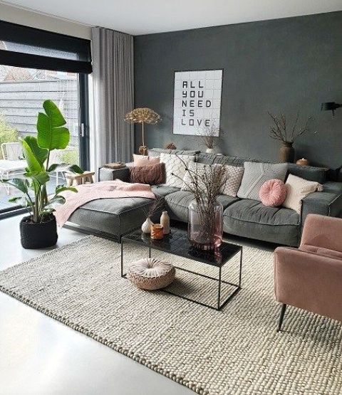 a spring-ready living room with a grey sofa, a pink chair, pillows and blankets, some branches in vases and a statement plant