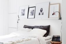 a white Nordic bedroom with a ledge with artworks, a comfy bed, wooden stools as nightstands and lamps