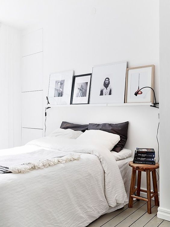 a white Nordic bedroom with a ledge with artworks, a comfy bed, wooden stools as nightstands and lamps