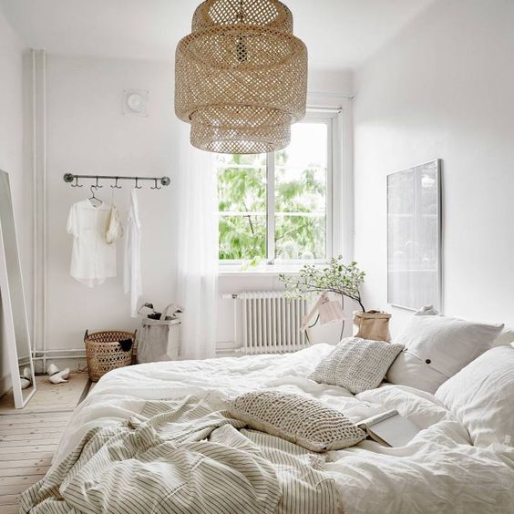 an airy Nordic bedroom with a wicker lampshade, crochet pillows, neutral furniture and much light