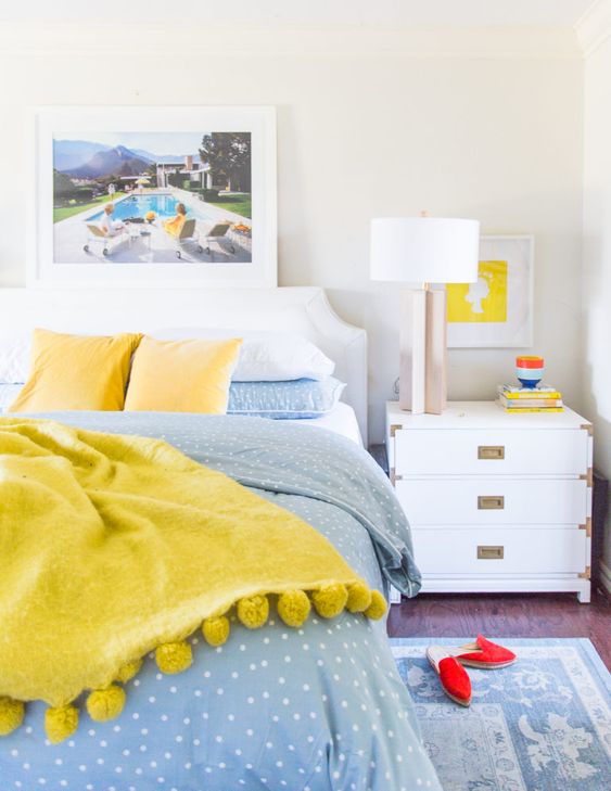 bright blue and sunny yellow bedding for a contrast and bold artworks make the space spring-summer-infused