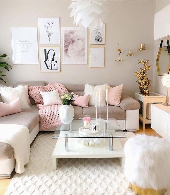 a beautiful feminine living room with dove grey walls, a corner sofa with pink and neutral blankets and pillows, lovely gold decor and a tiered coffee table