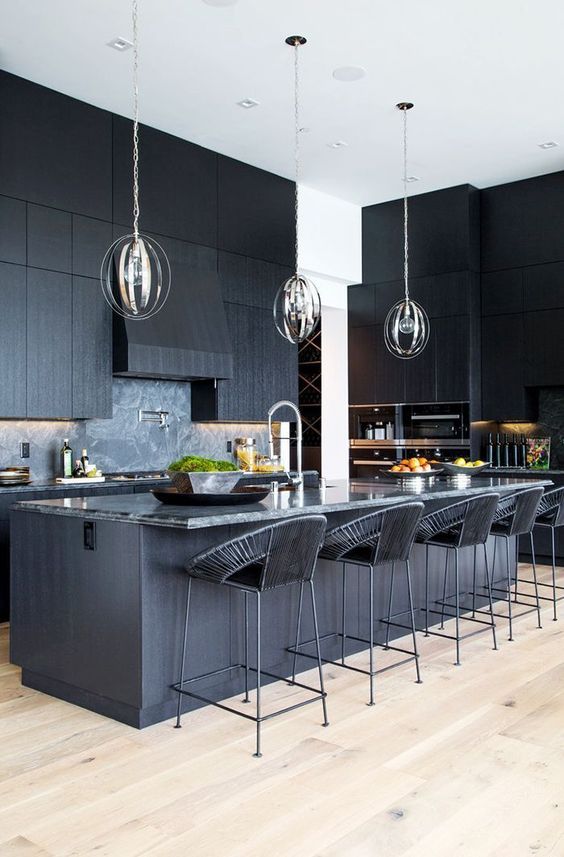 a black kitchen with textural cabinets, a kitchen island with a stone countertop and woven stools plus pendant lamps
