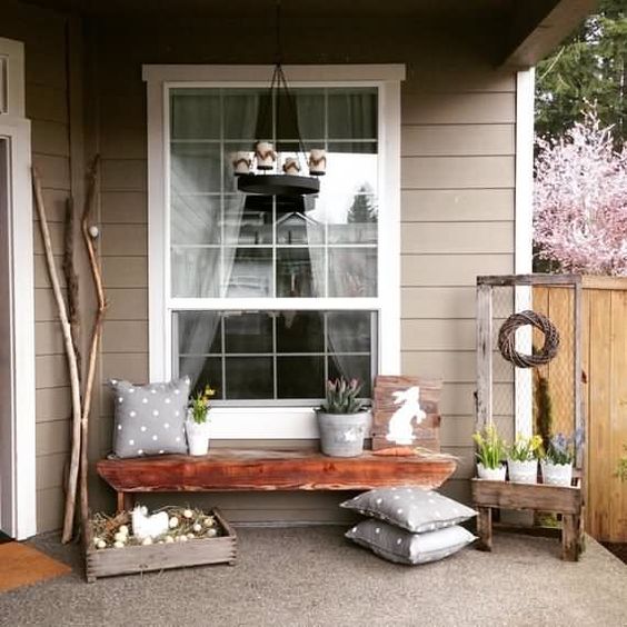 a chic Easter porch with polka dot pillows, a bunny sign, potted blooms and a crate with eggs and a fake hen