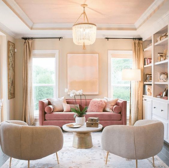 a chic and modern living room with neutral built-in furniture, neutral chairs and a pink sofa, a round table and a beaded chandelier is cool