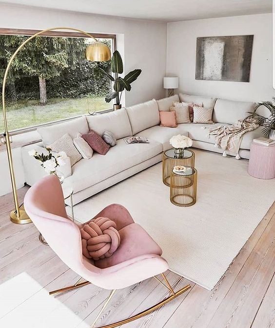 a chic contemporary living room with a feminine feel, a large corner sofa, a blush rocker and a pouf, pink pillows and a gold floor lamp